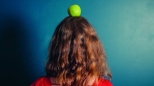 eine Person mit langen Haaren von hinten mit einem Apfel auf dem Kopf