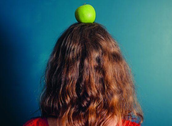 eine Person mit langen Haaren von hinten mit einem Apfel auf dem Kopf